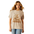 Woman wearing a beige t-shirt with a graphic design of a cow and the brand 'Ariat' on a white background.